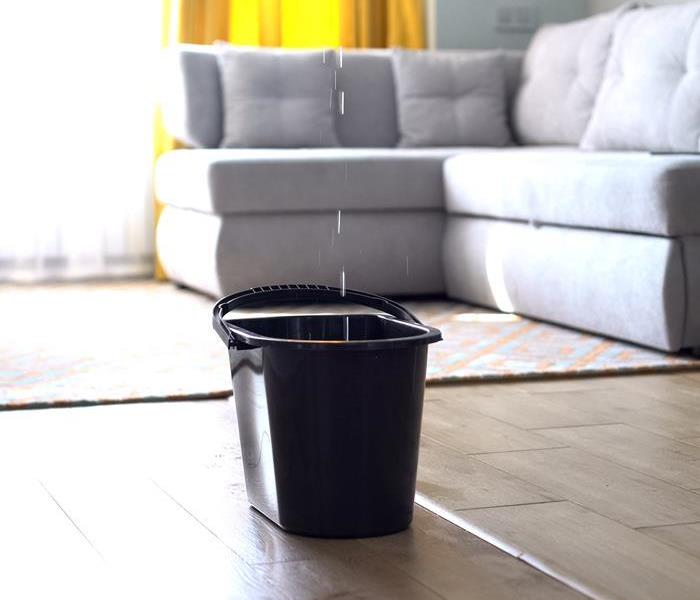 A bucket in a living room catching dripping water. 